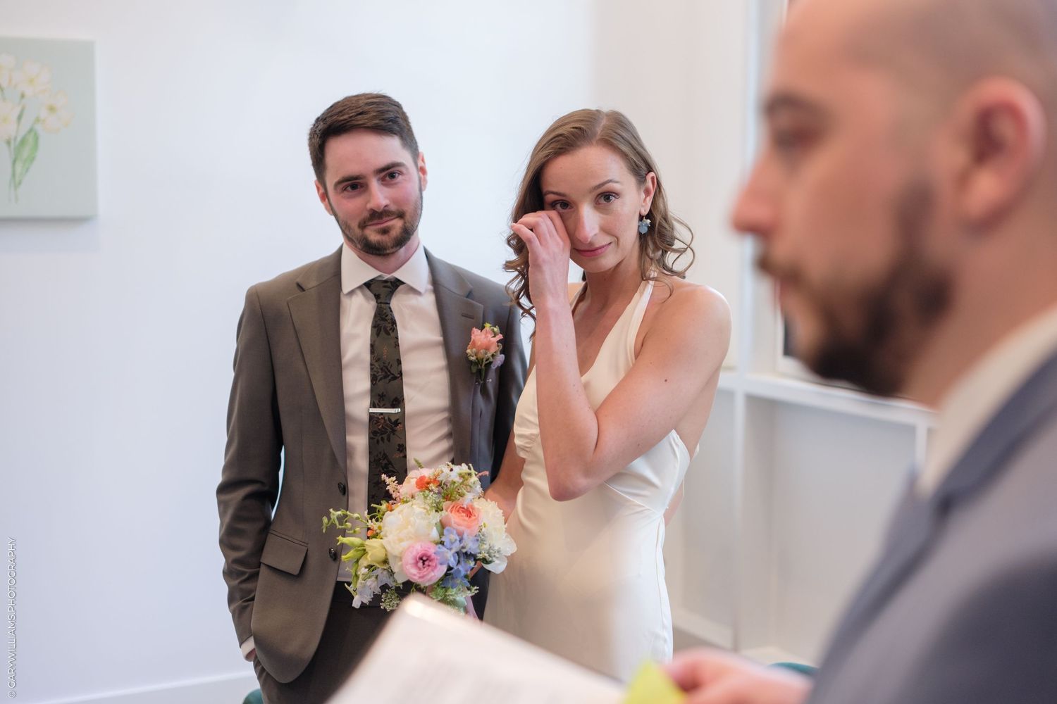 A candid wedding moment captured during the ceremony shows emotional expressions while holding a colorful floral bouquet.