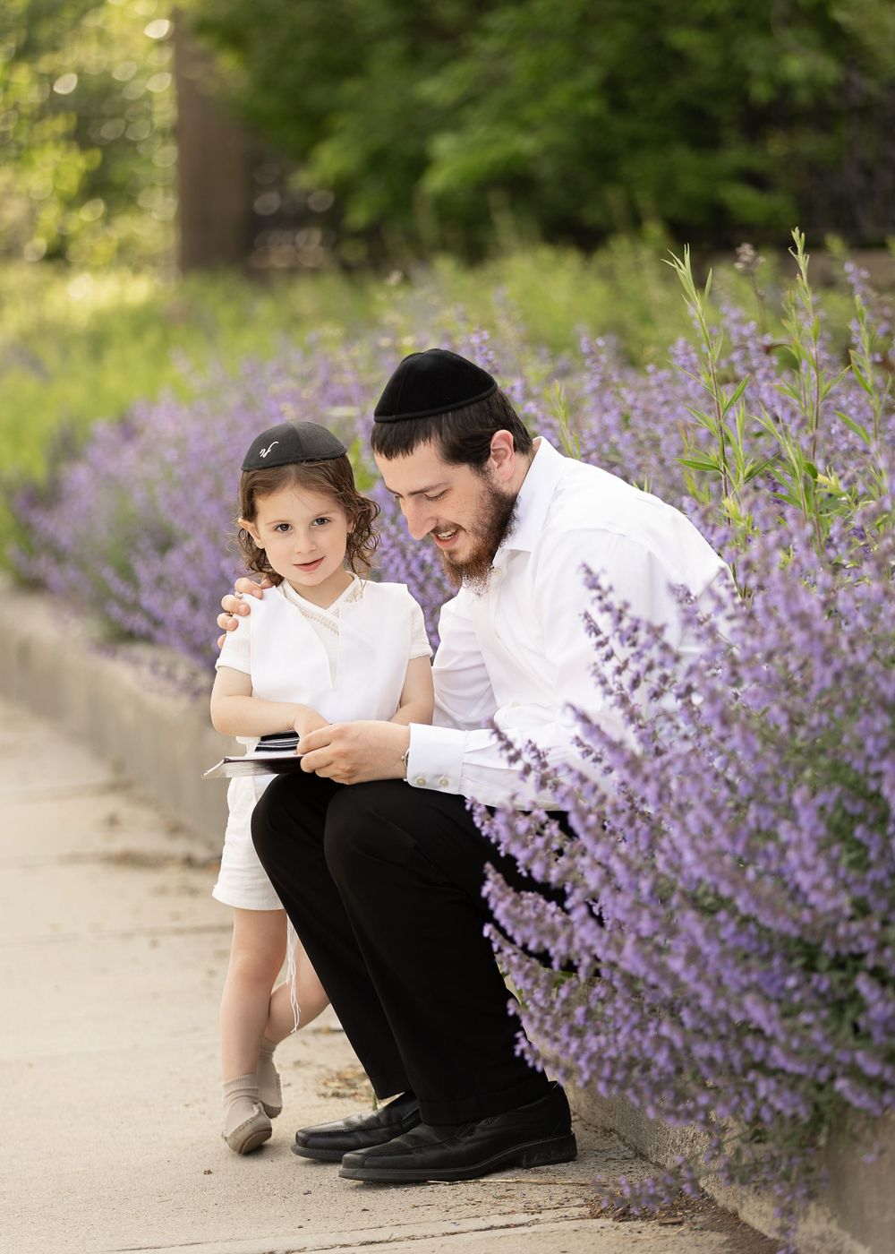 Two people sit together on a garden path with beautiful purple lavender flowers blooming beside them.