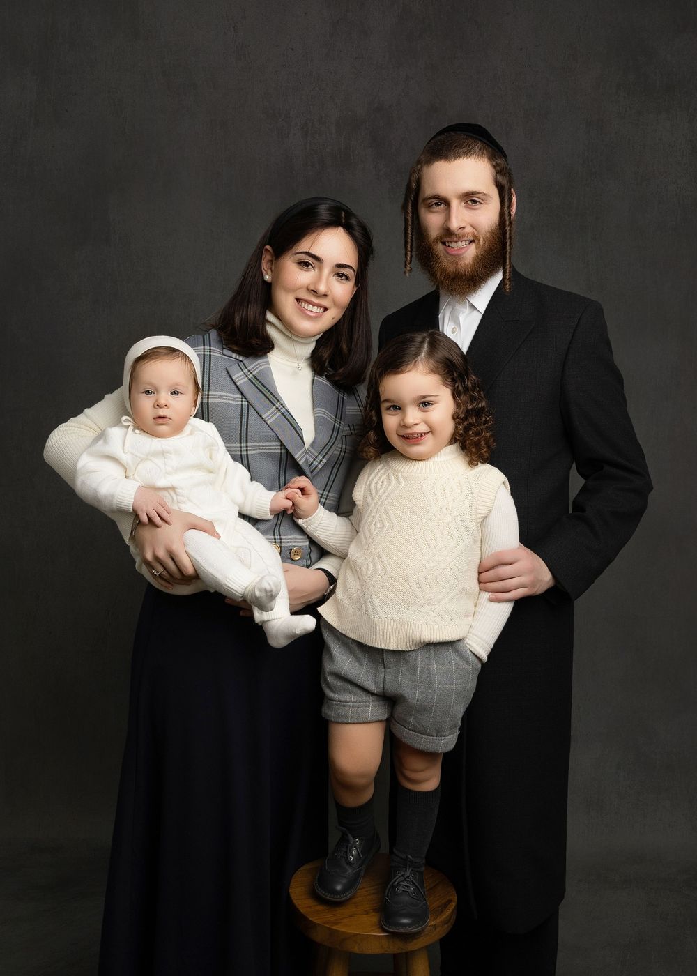 Professional studio portrait series showing a family in coordinated outfits against a dark backdrop.