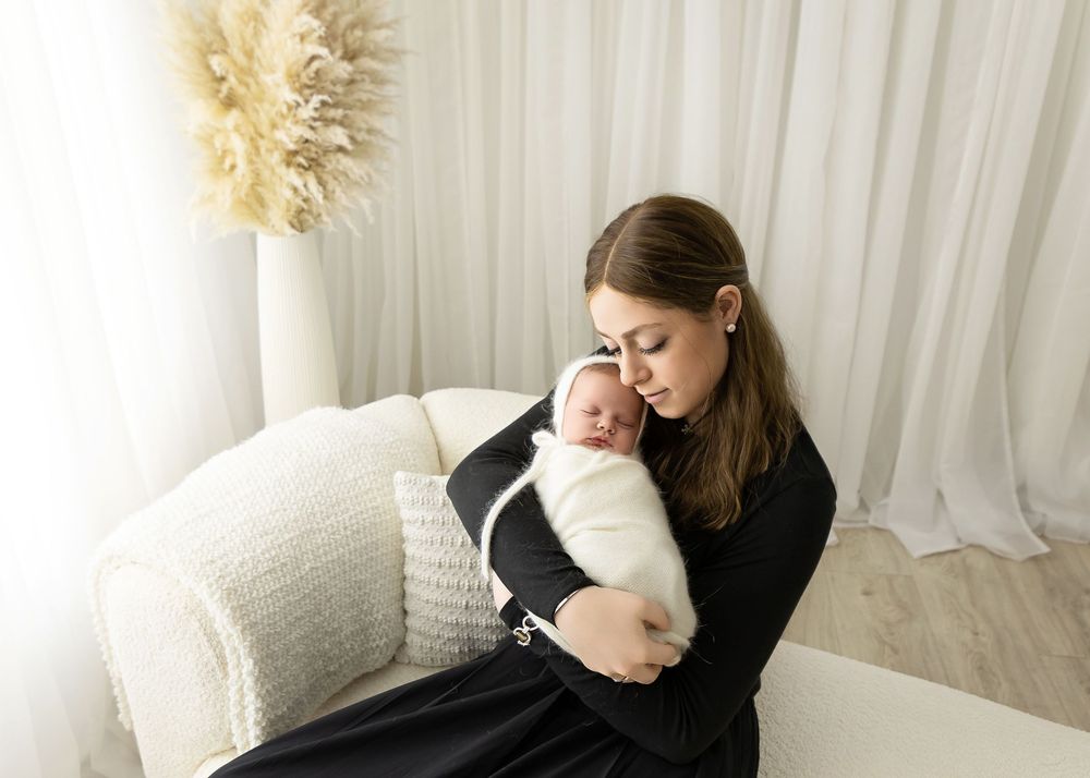 Intimate moment between mother and newborn on white couch with cream-colored pampas grass decor.