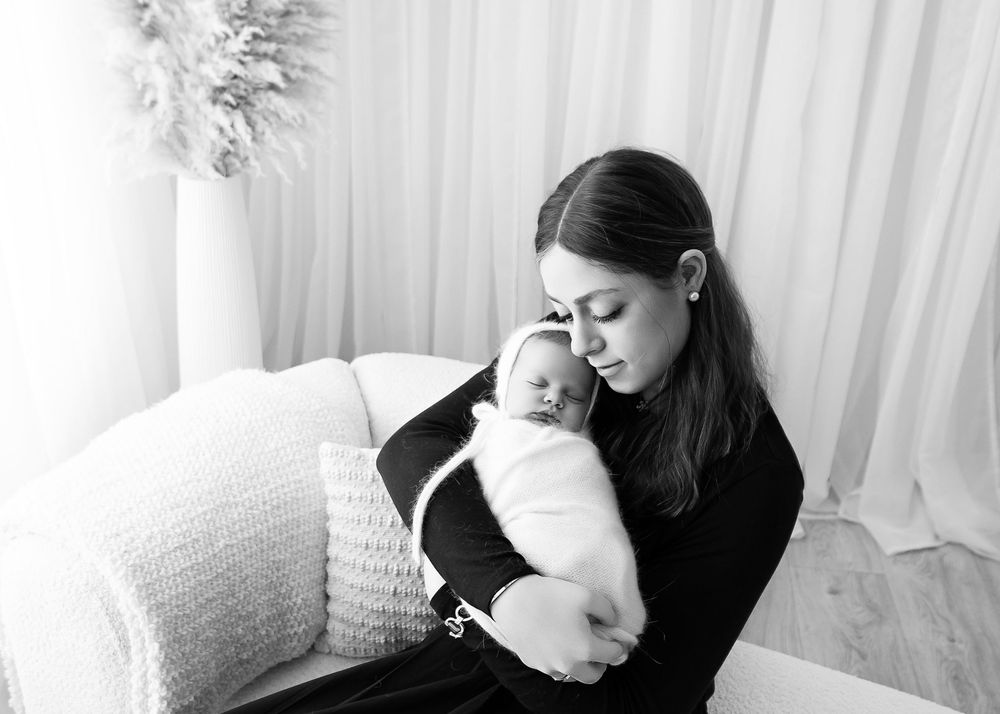 Black and white portrait of tender moment between mother and sleeping newborn on couch.
