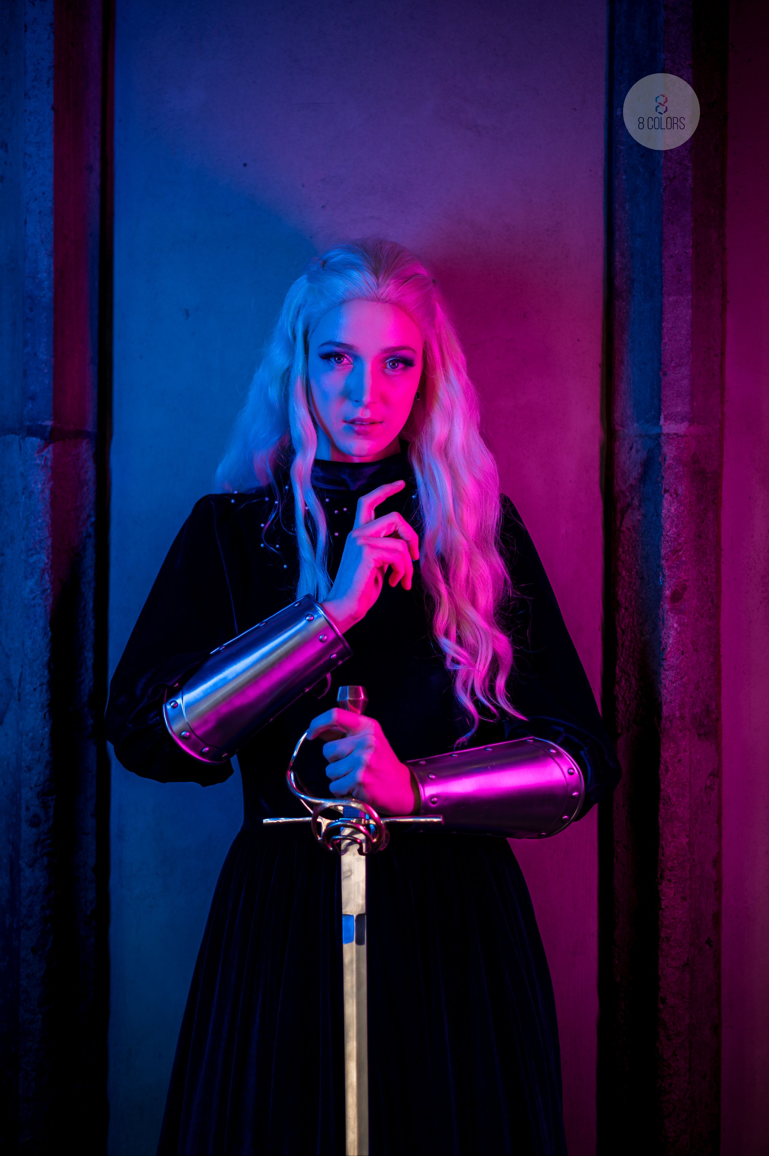 Atmospheric portrait with neon blue and pink lighting illuminating a figure in black dress holding metallic cups against dark background.