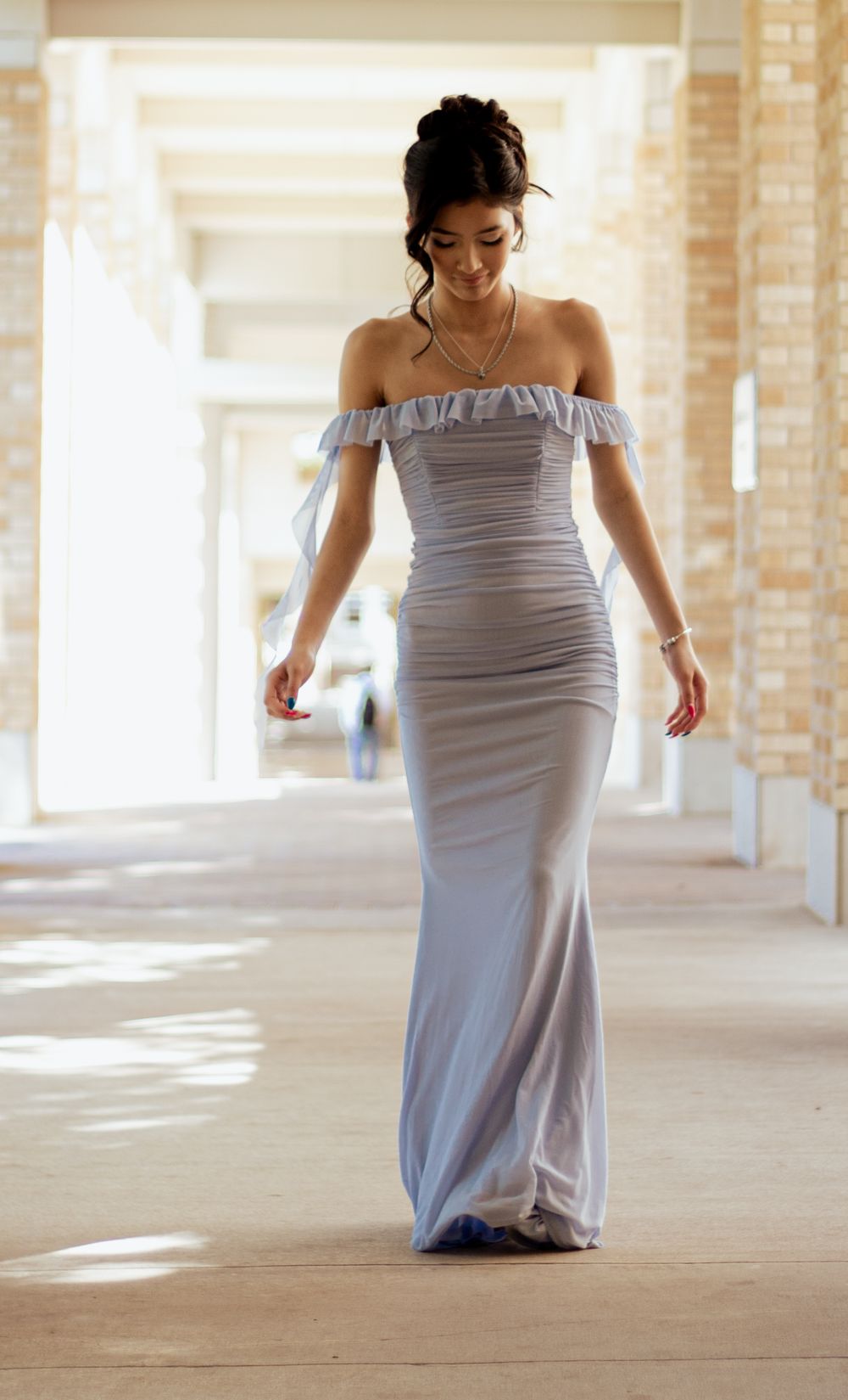 Elegant silver-gray off-shoulder mermaid gown with ruched detailing flows gracefully in a sunlit corridor.