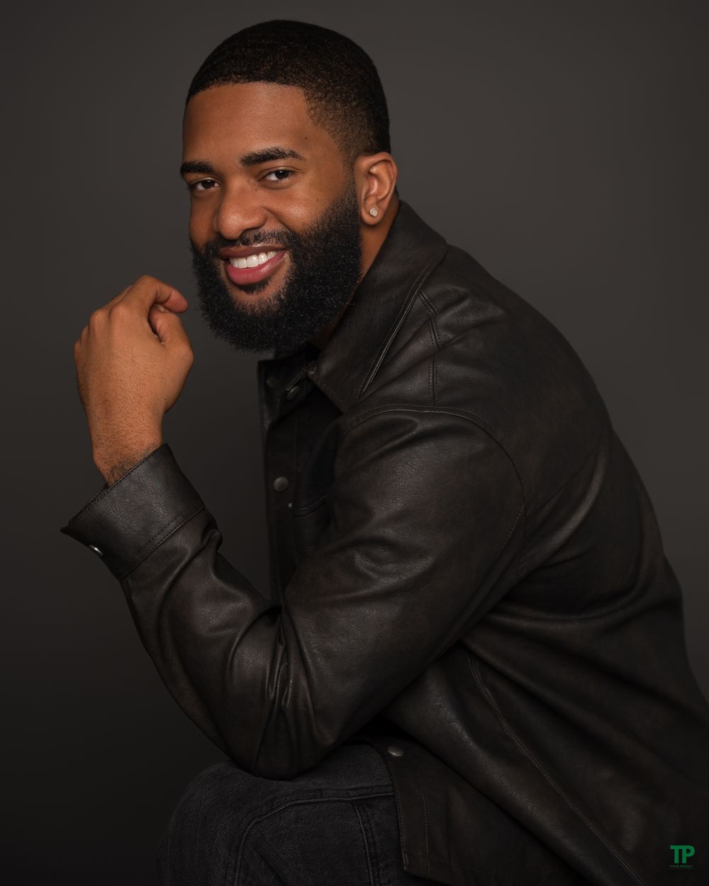 Professional portrait of someone in a black leather jacket against dark background with warm lighting and genuine smile.