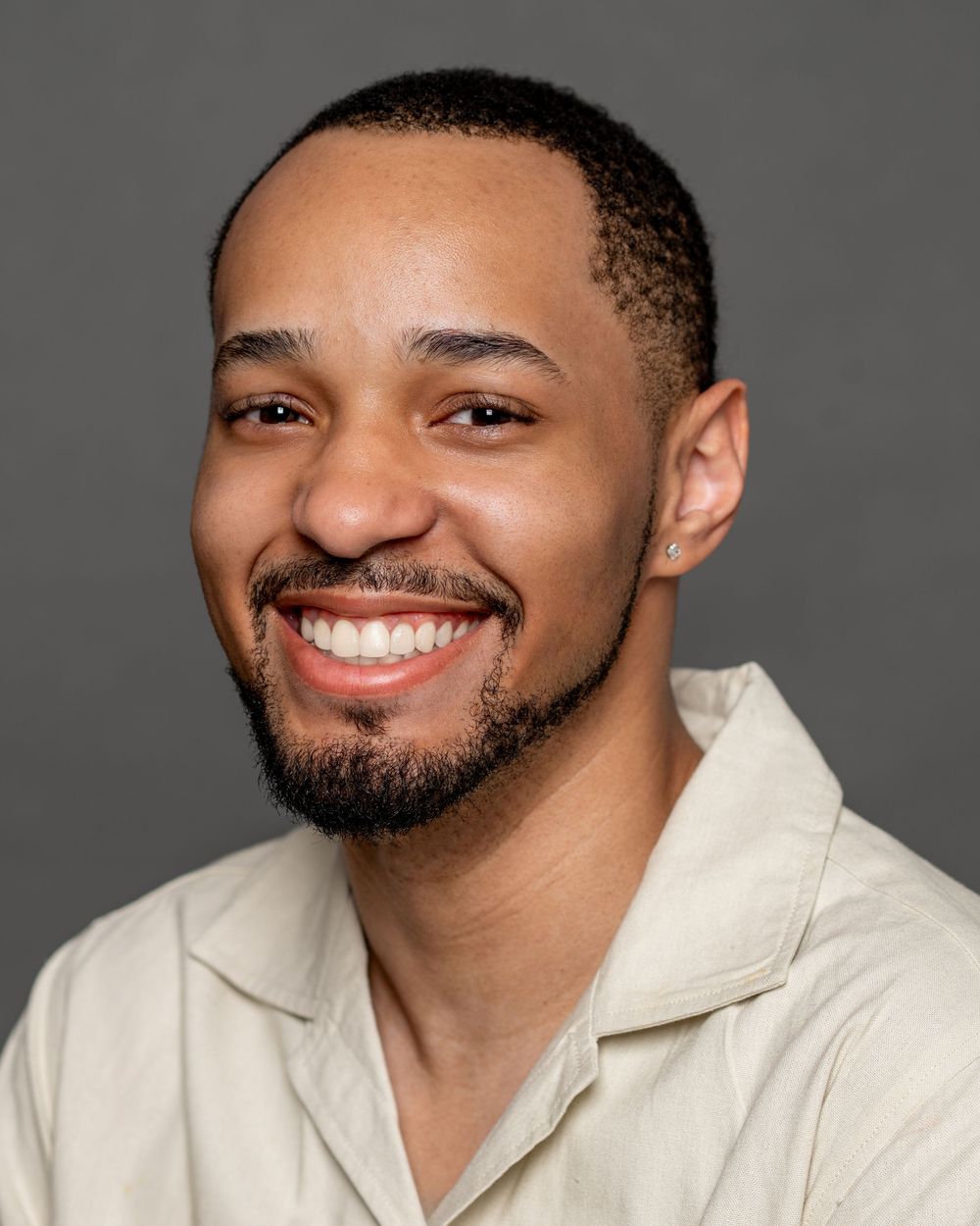 A person in a white collared shirt smiles warmly against a gray studio backdrop.