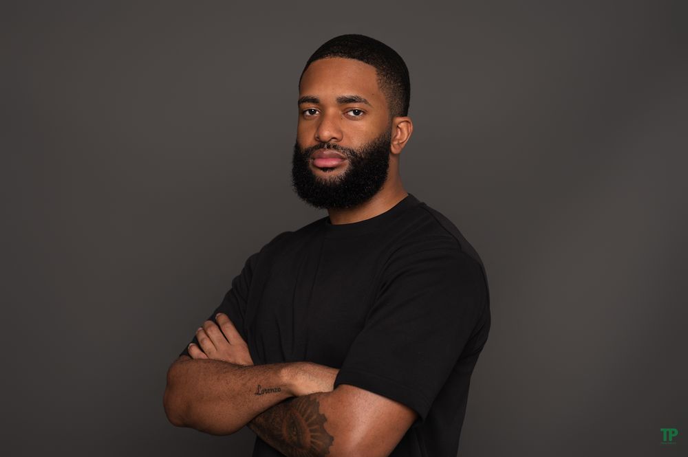 Professional studio portrait of someone in a black t-shirt with crossed arms against a dark gray background.