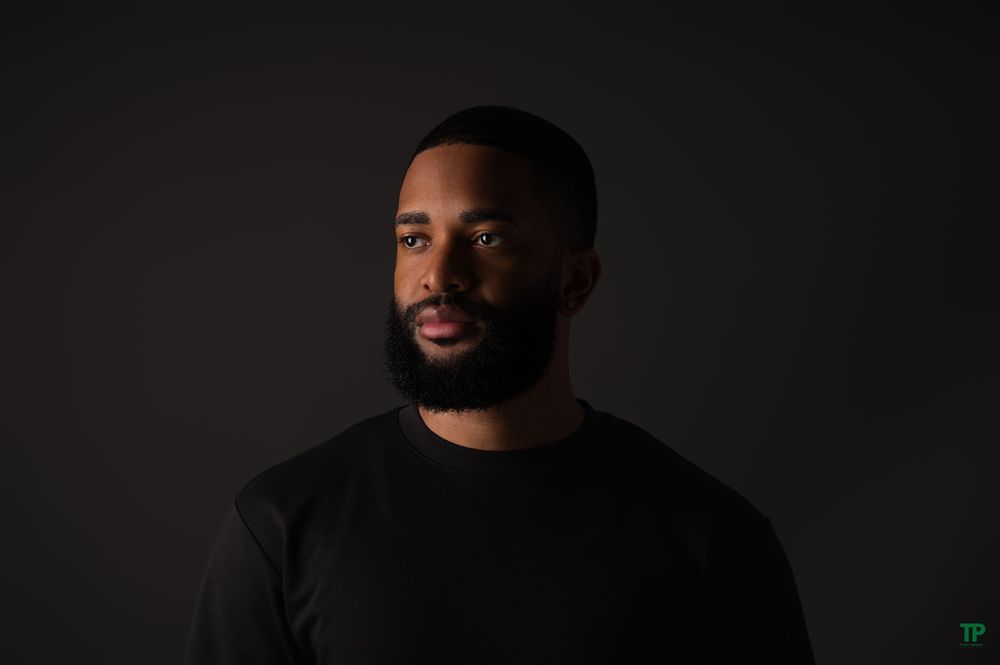 Portrait of someone wearing a black sweater against a dark background with dramatic lighting.
