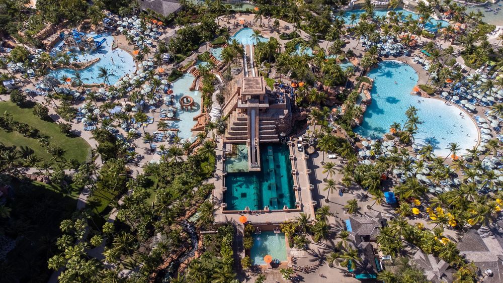 Panoramic aerial shot of a coastal resort with multiple swimming pools and palm trees.