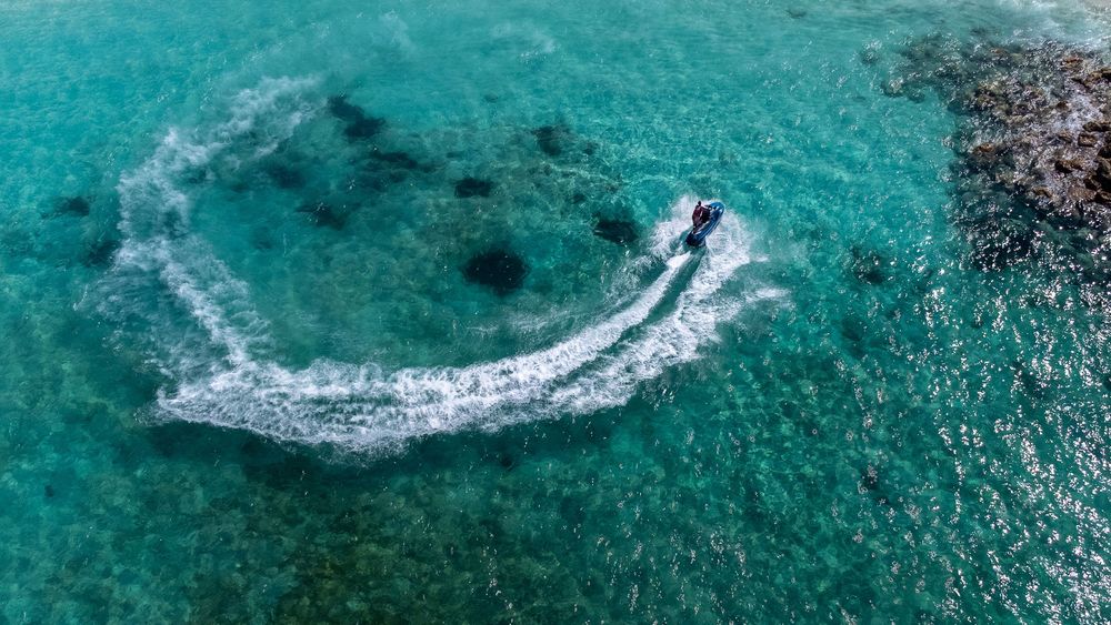 Aerial view of turquoise ocean water with boat wake patterns visible from above.