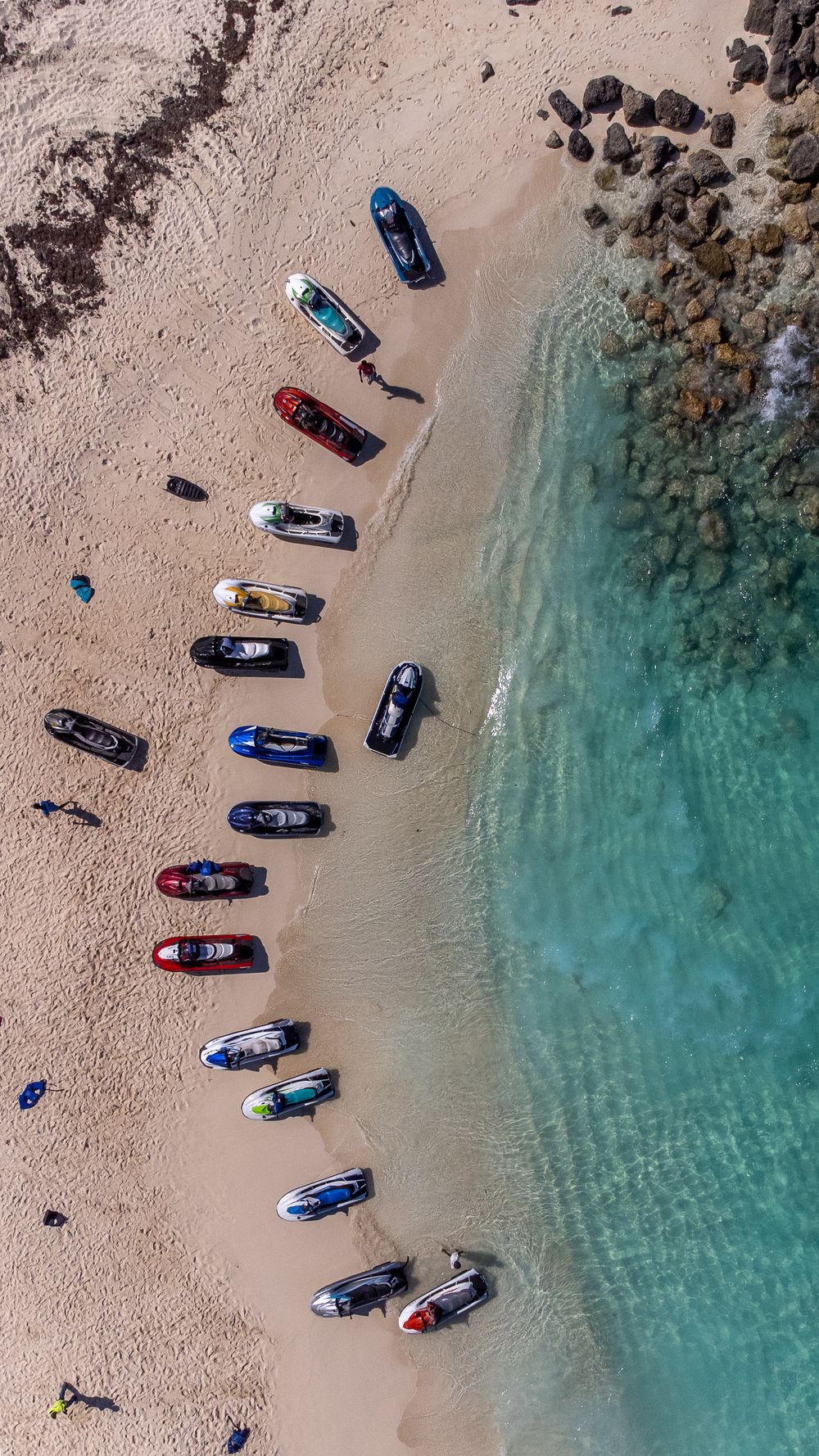 Aerial view of boats parked on sandy beach next to crystal clear turquoise waters.