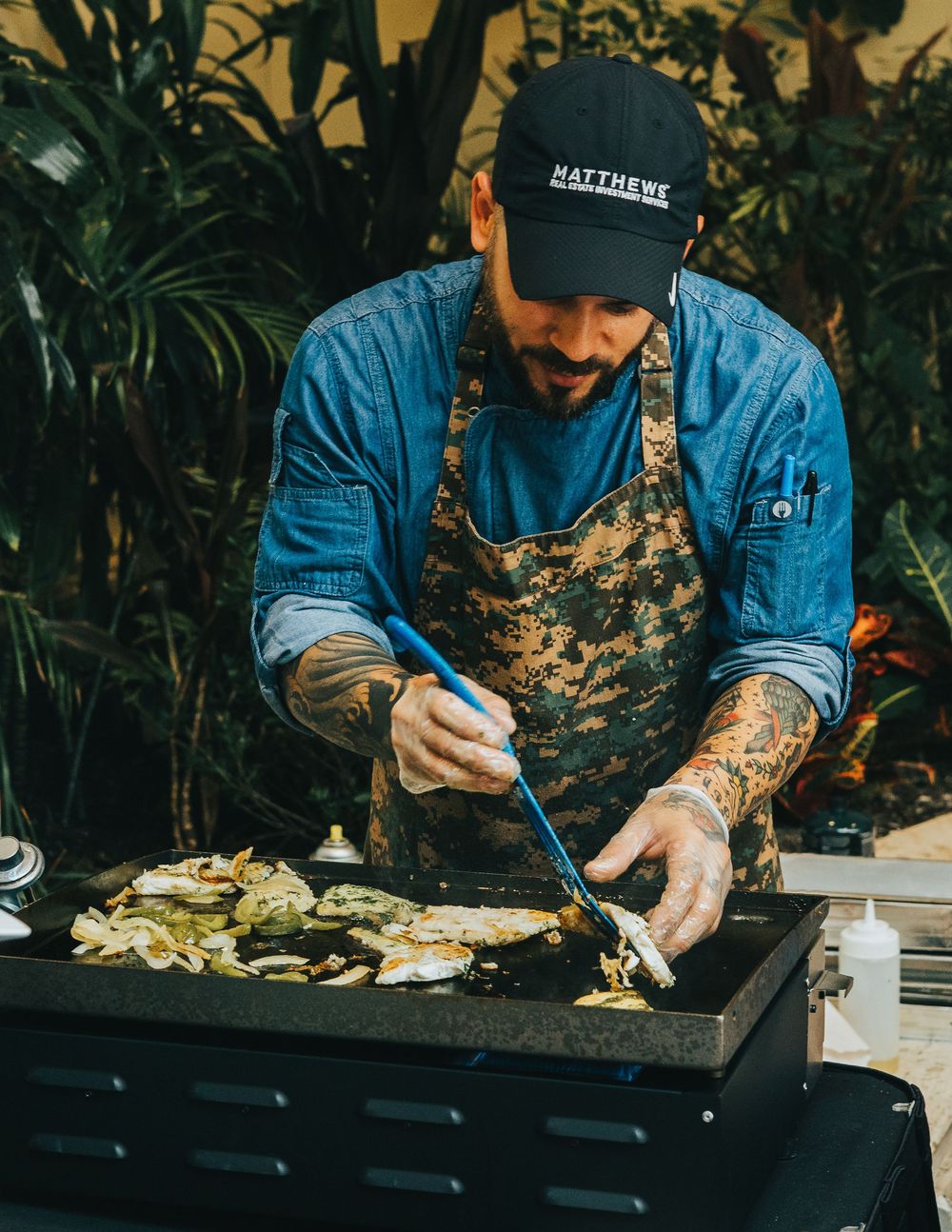 Chef preparing food on a black grill at an outdoor cooking station.