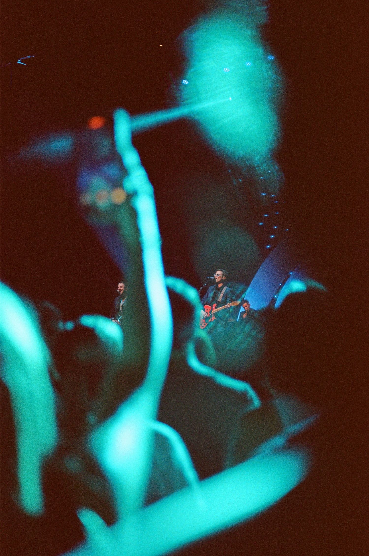 Saint Motel during a concert on 35mm film, shows a shot through the crowd of the singer holding a guitar and singing. Concerts, San Diego