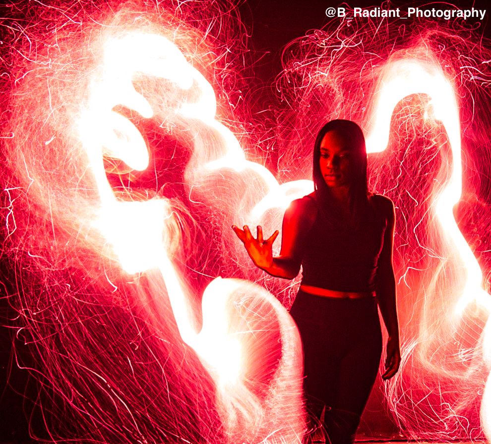 A dramatic silhouette against bright red light trails and sparks during a long exposure night photography shoot.
