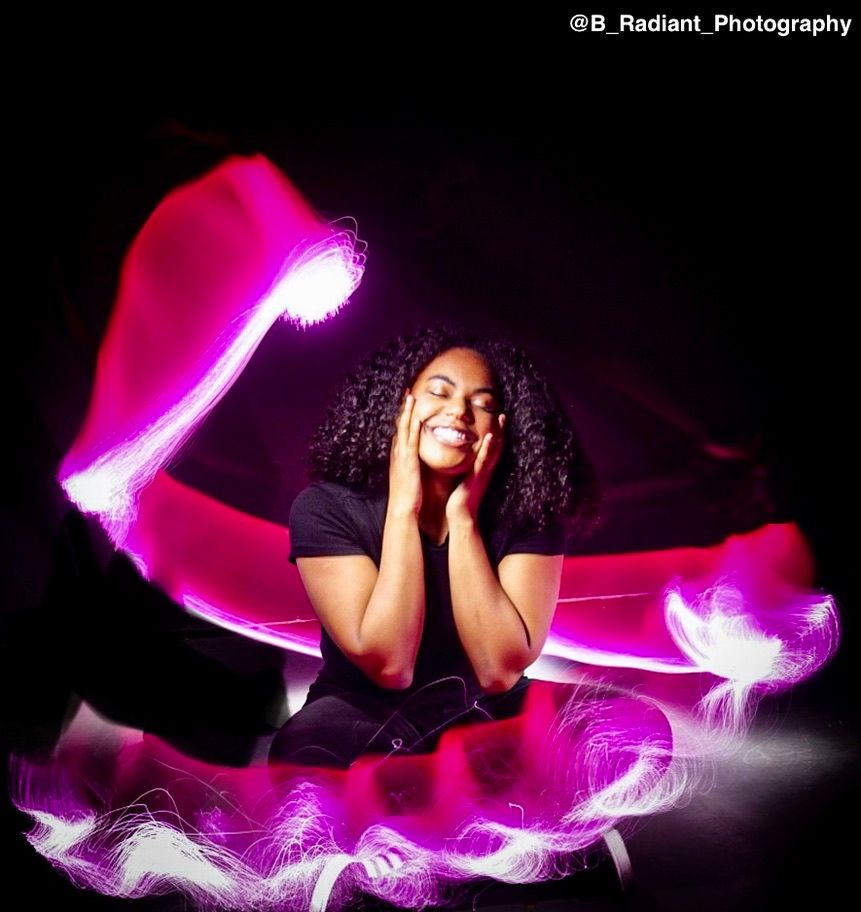 A figure draped in flowing pink and purple fabric creates a dramatic silhouette against a dark background.