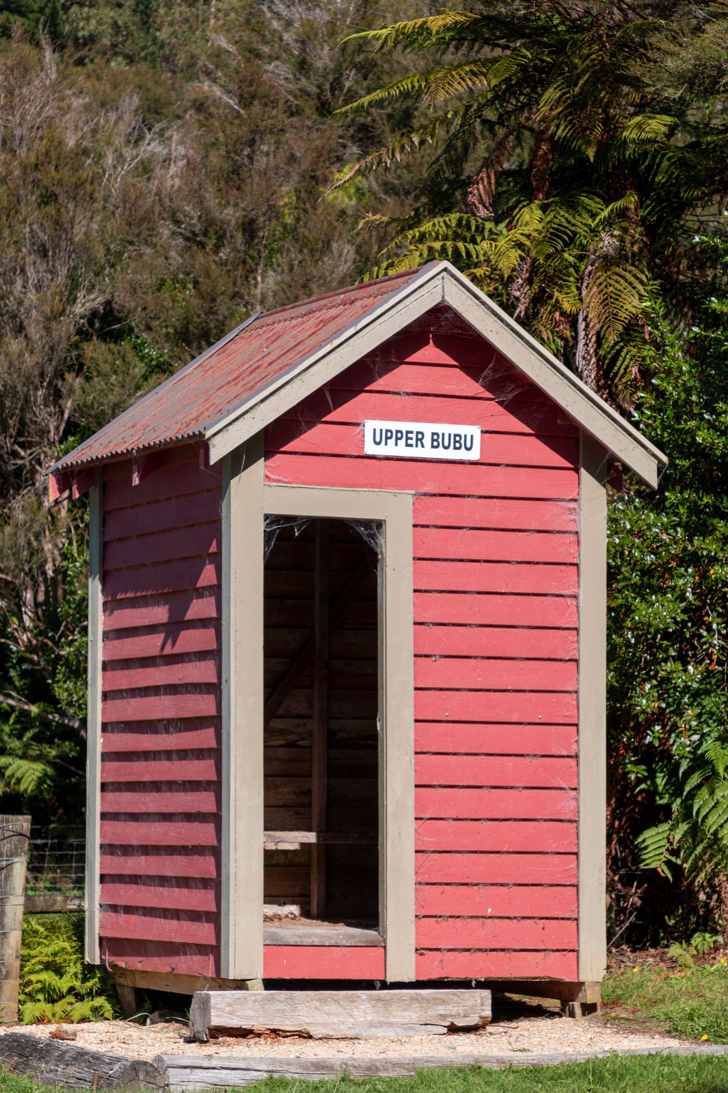 Small red wooden hut with a sign reading 'Open Cabin', set in greenery with trees in the background on a sunny day.