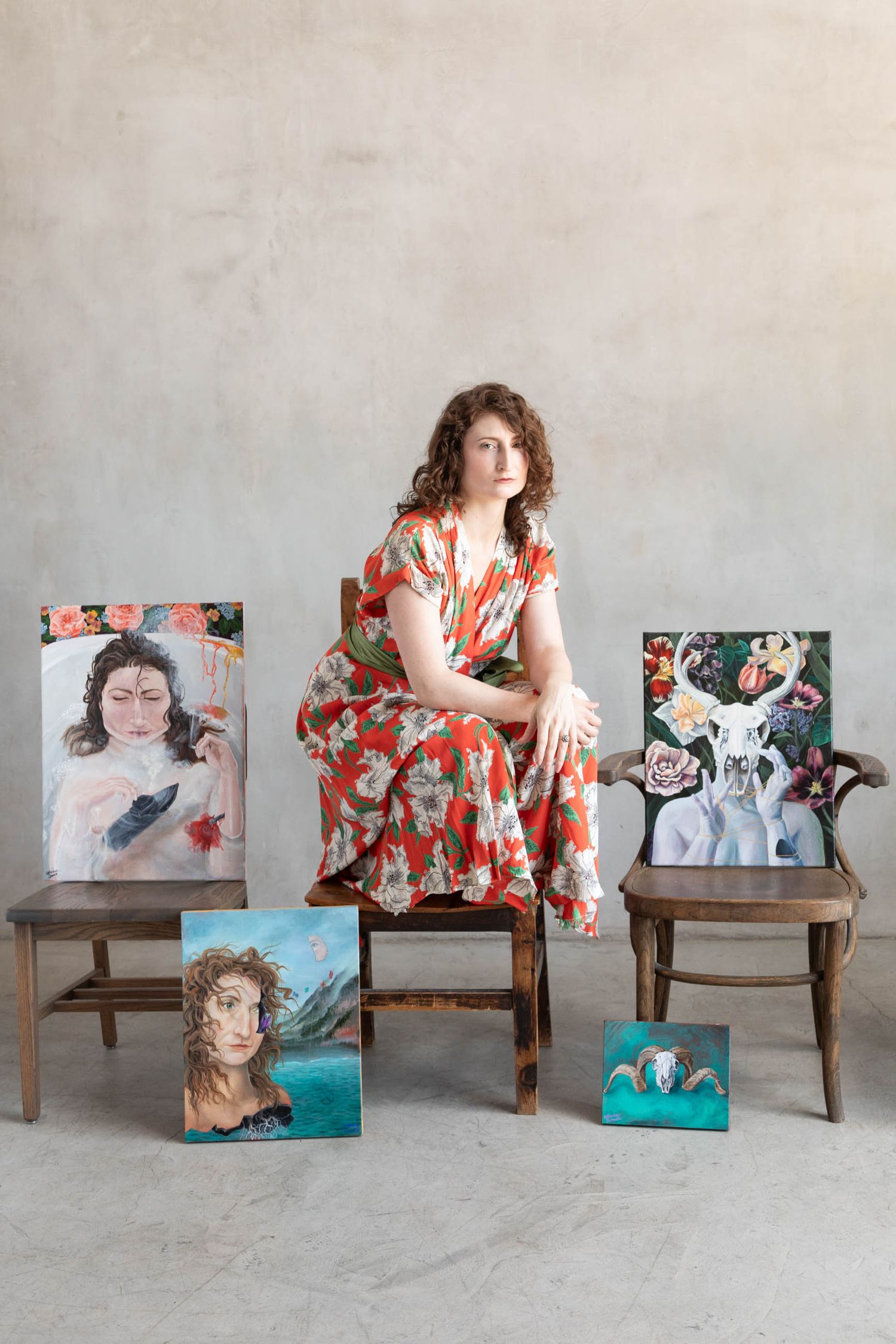 Woman standing on a chair in a studio, surrounded by her paintings