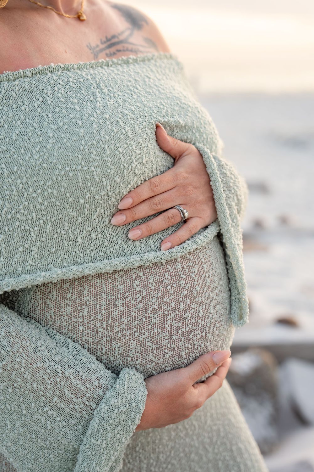 Close-up of pregnant belly held gently by hands wearing rings in mint knit dress.