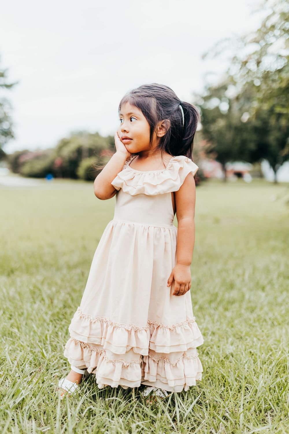 A sweet moment captured outdoors of a little one wearing a vintage-style ruffled cream dress in a grassy field.