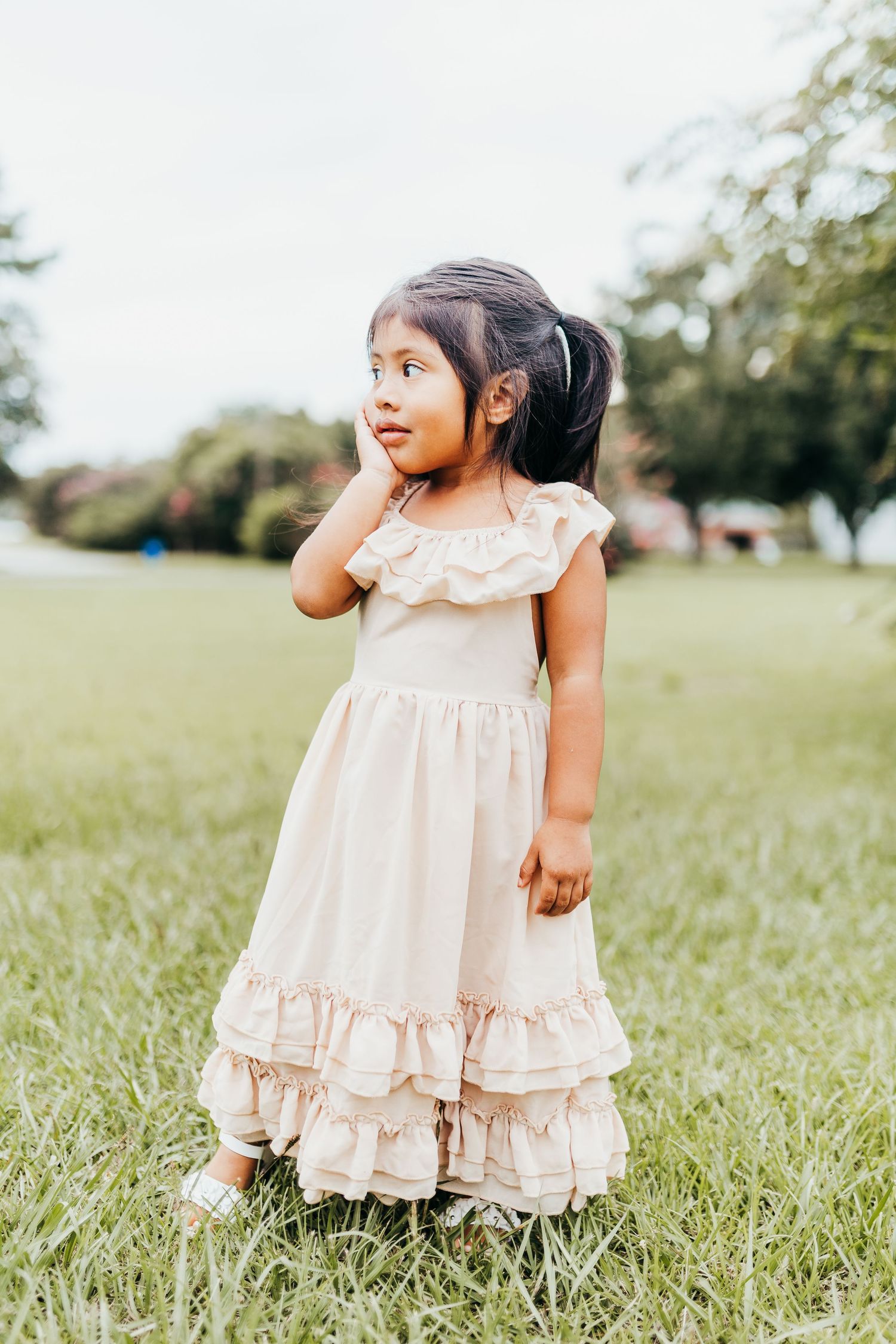 A sweet moment captured outdoors of a little one wearing a vintage-style ruffled cream dress in a grassy field.