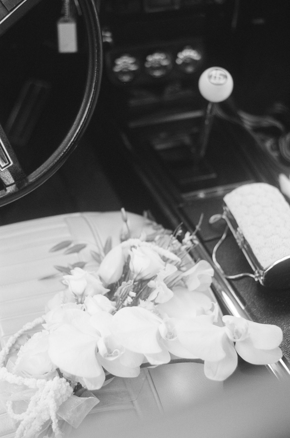 White orchids arranged on a car's dashboard in black and white photography.
