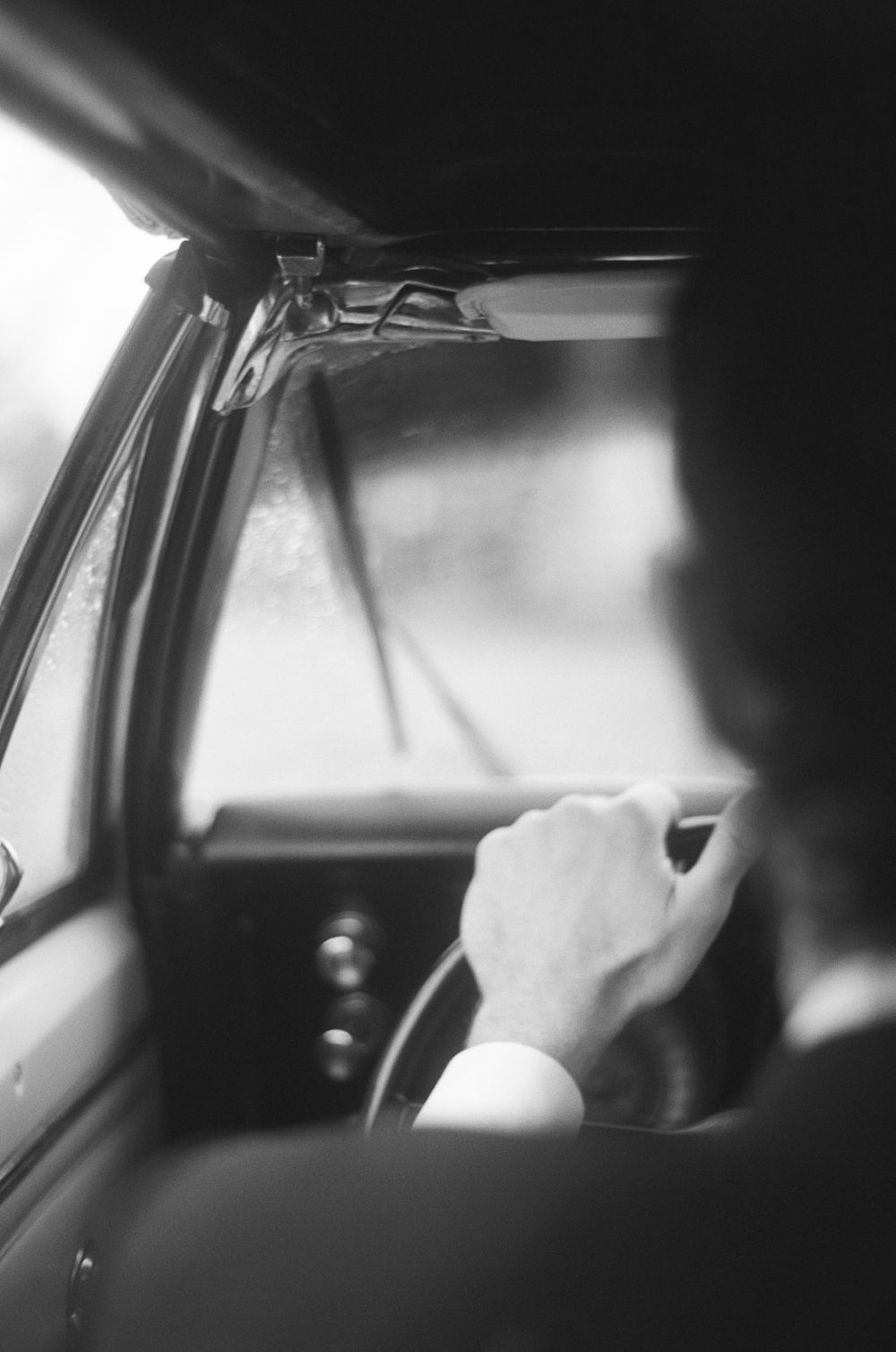 Black and white photograph of someone in a wedding dress entering a vintage car.