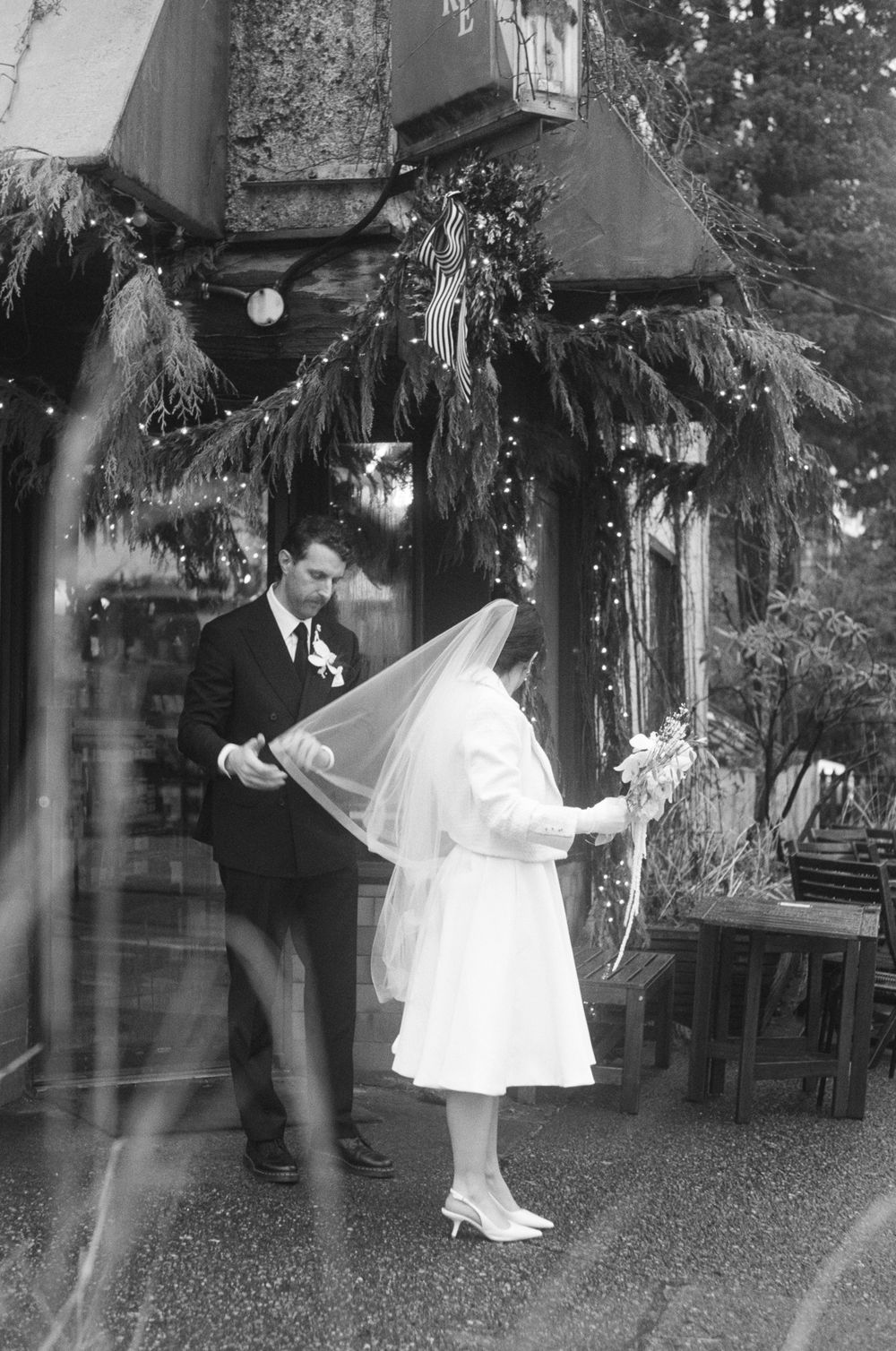 Black and white wedding scene with decorative lights and trees in an outdoor setting.