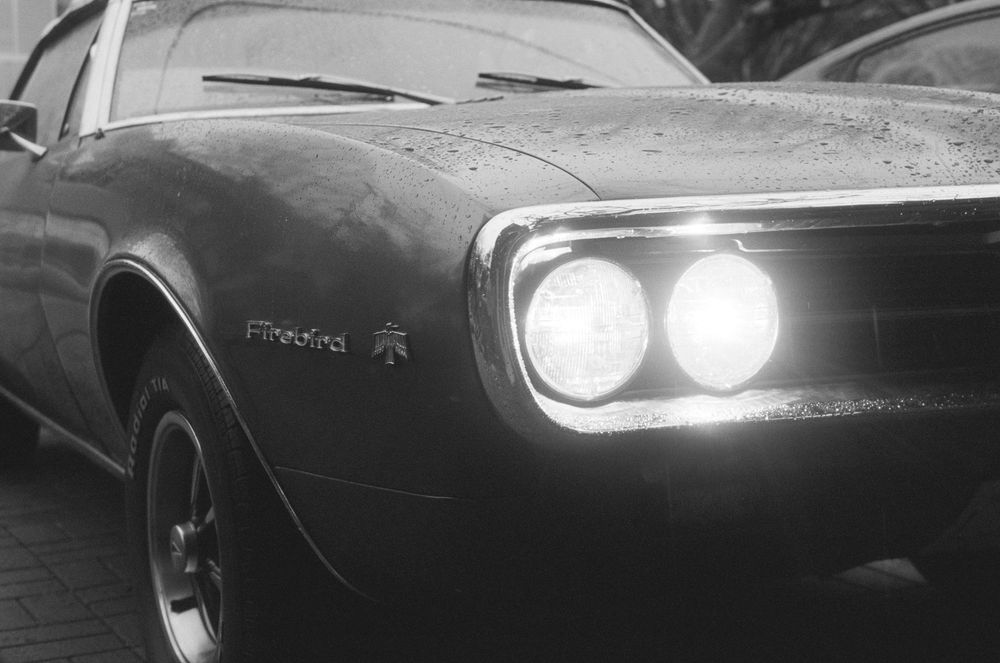 Vintage car headlights illuminated in black and white photography.