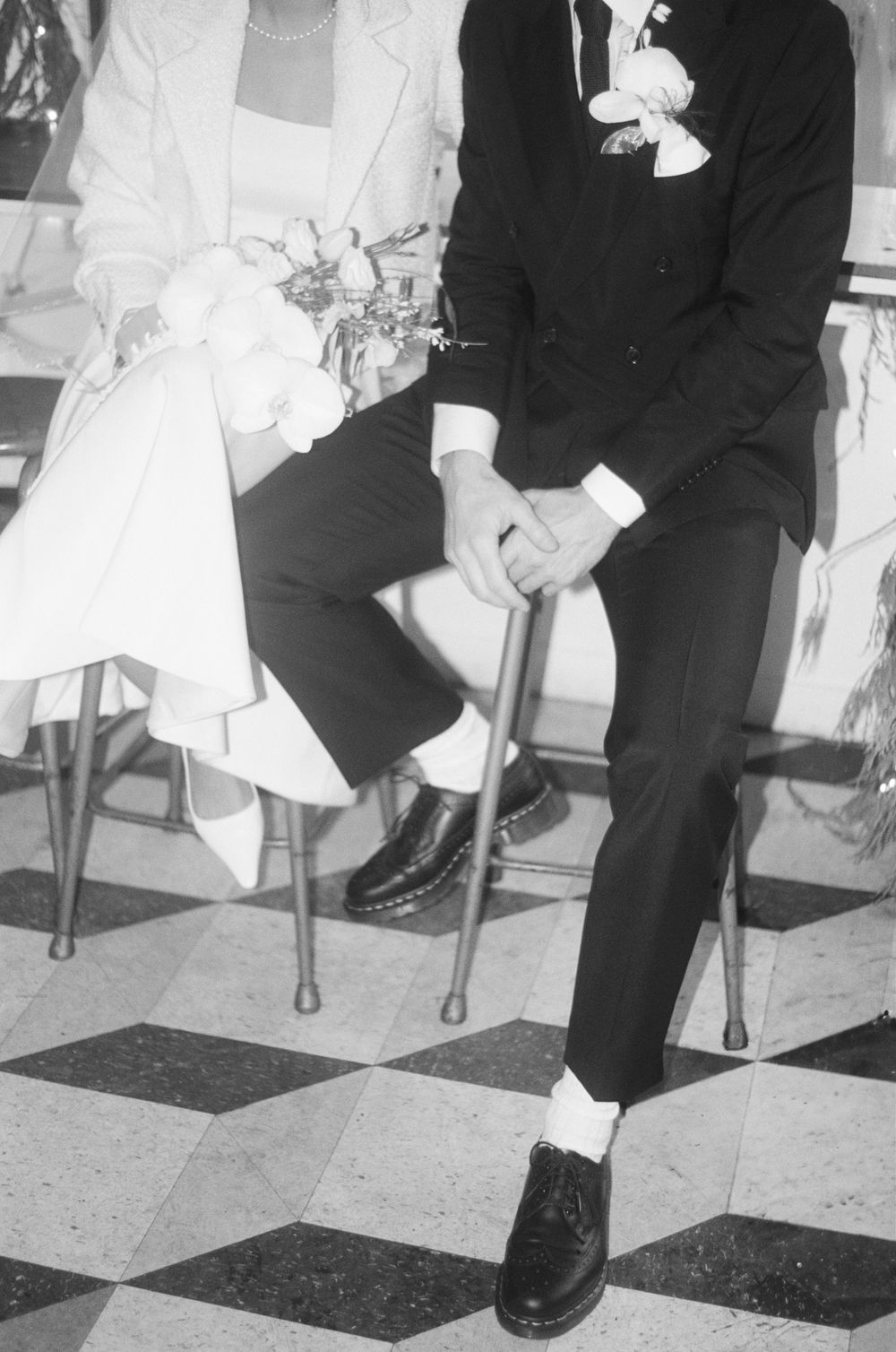 Black and white photograph showing formal shoes and attire on a checkered floor.