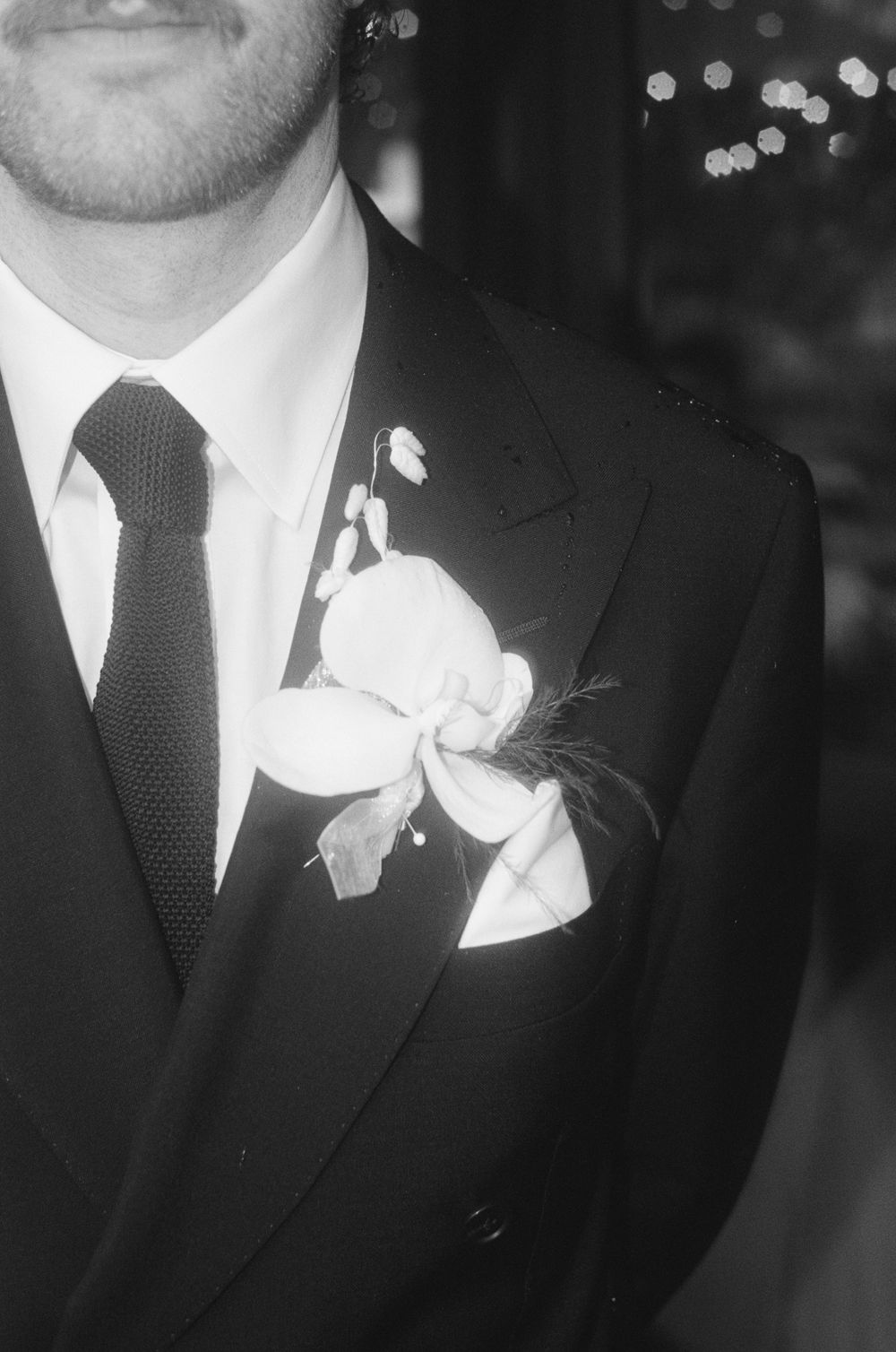 Black and white close-up of groomsmen in formal suits with white boutonnieres against a dark background.