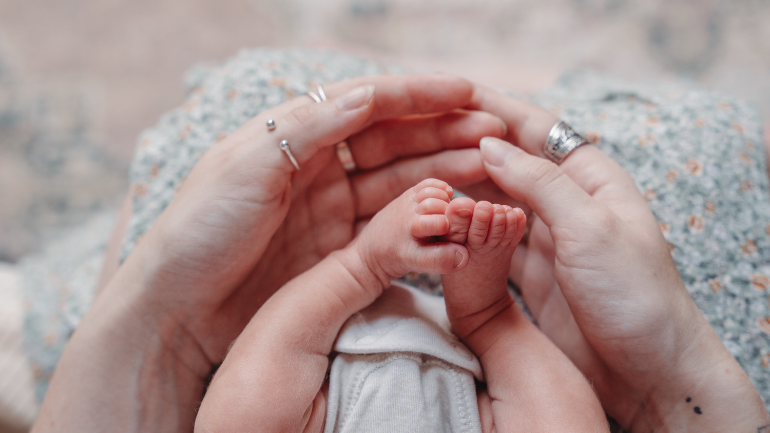 Adult hands gently holding tiny baby hands in a tender moment.