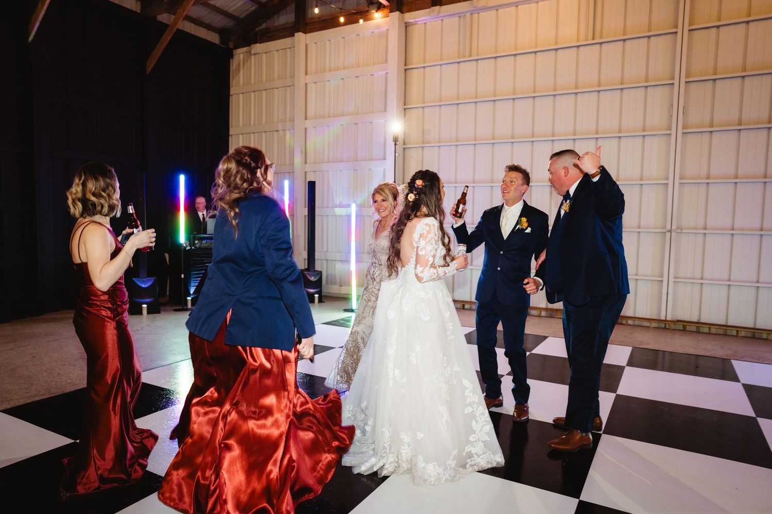 Couples dancing together on a black and white checkered dance floor at an indoor wedding reception.