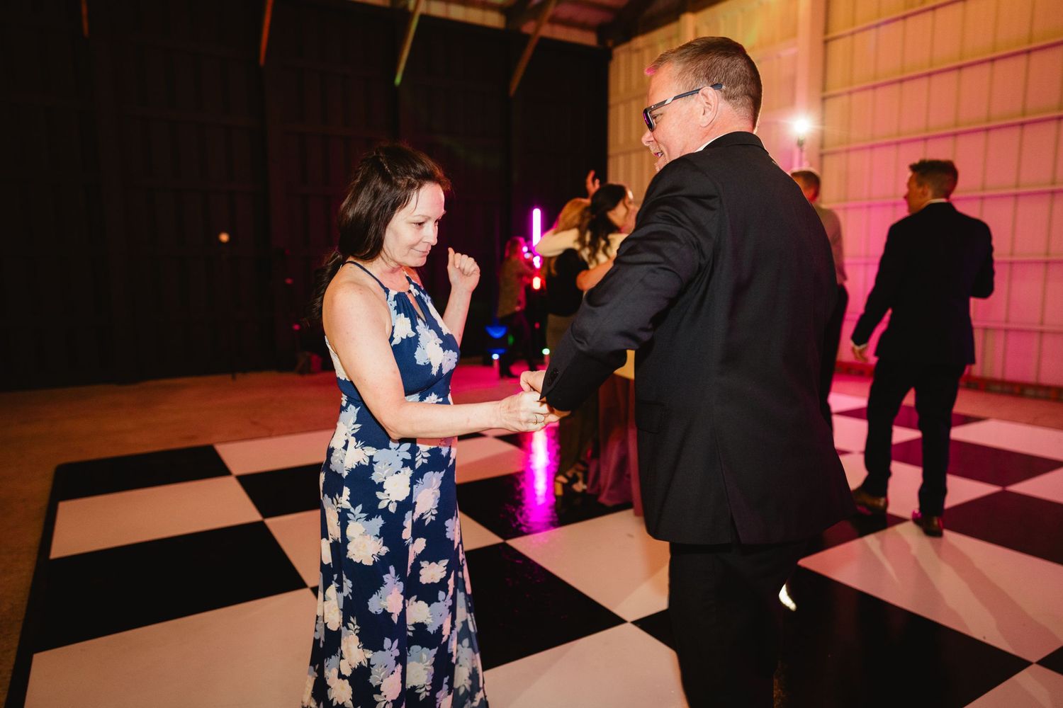 Two people dancing together on a black and white checkered dance floor with pink lighting in the background.