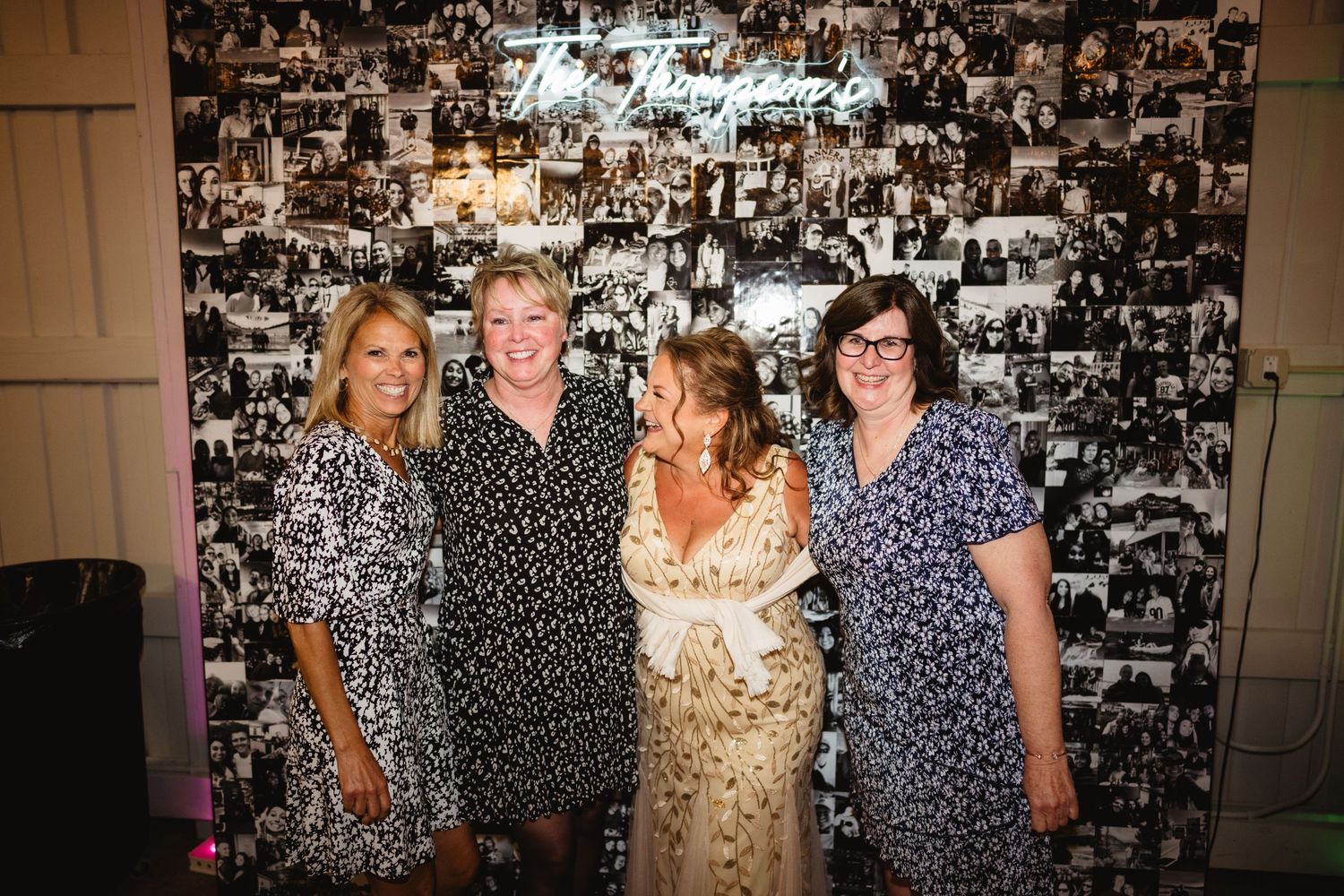 Four people pose together in front of a wall covered in black and white photographs at a special event.