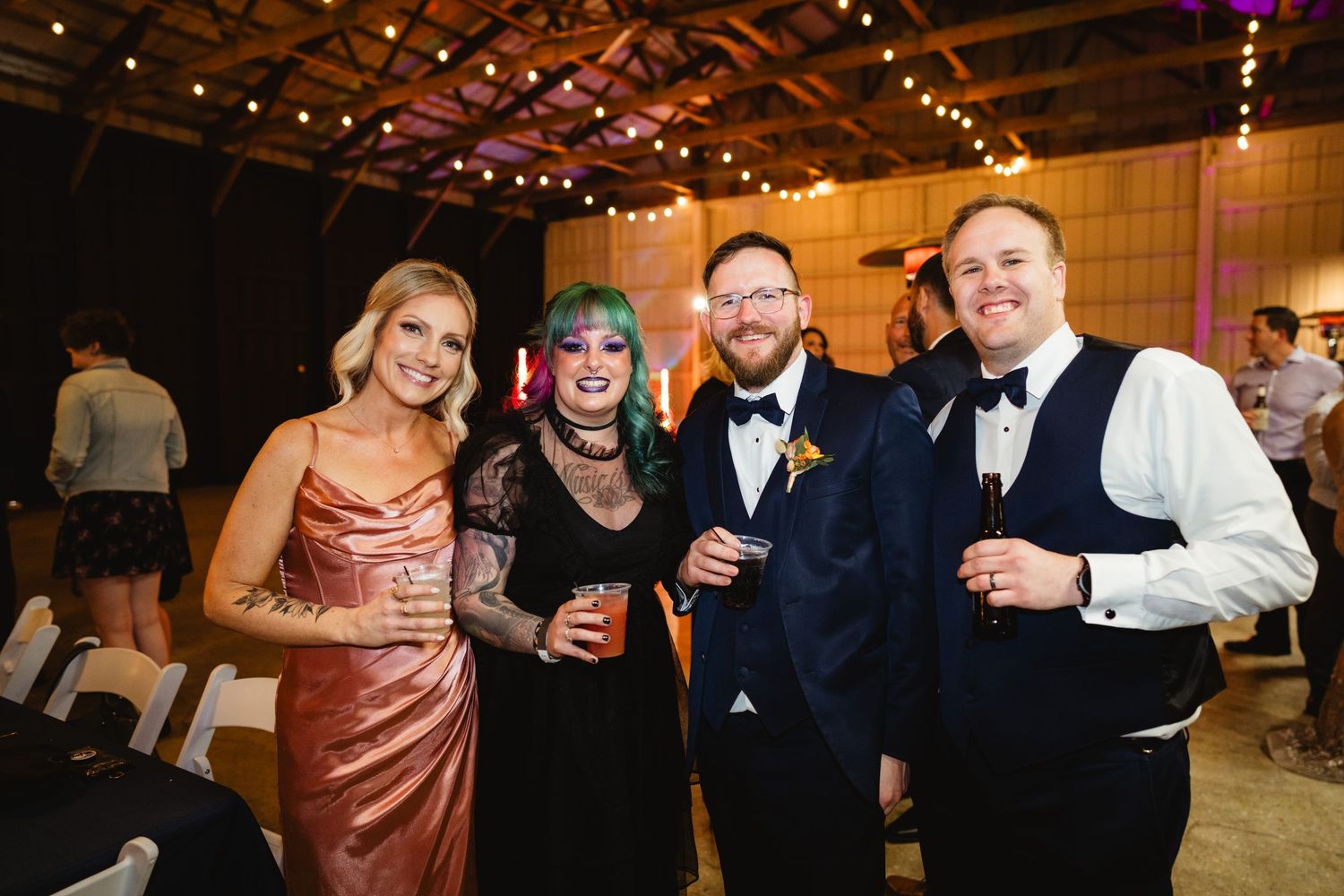 Wedding guests in formal attire smile and socialize during an elegant reception with string lights overhead.
