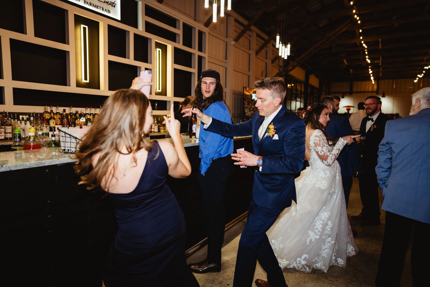 Wedding guests dance and celebrate at the bar area of the reception venue.
