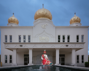 Panoramic view of a white Sikh Gurdwara in Houston with golden domes and reflecting pool with the Bride and Groom posing.