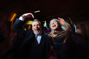 Two people dancing energetically at wedding reception with colorful lights in the background and shutter drag effect.