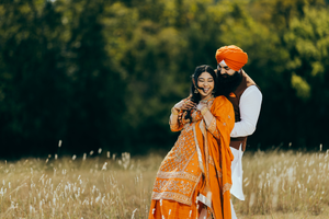 Sikh couple in vibrant orange traditional attire photographed in sunny meadow in Austin, TX.