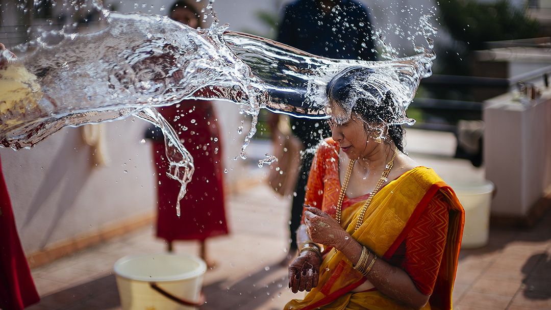 Woman in yellow sari getting water poured over her head during a traditional Indian Haldi celebration.