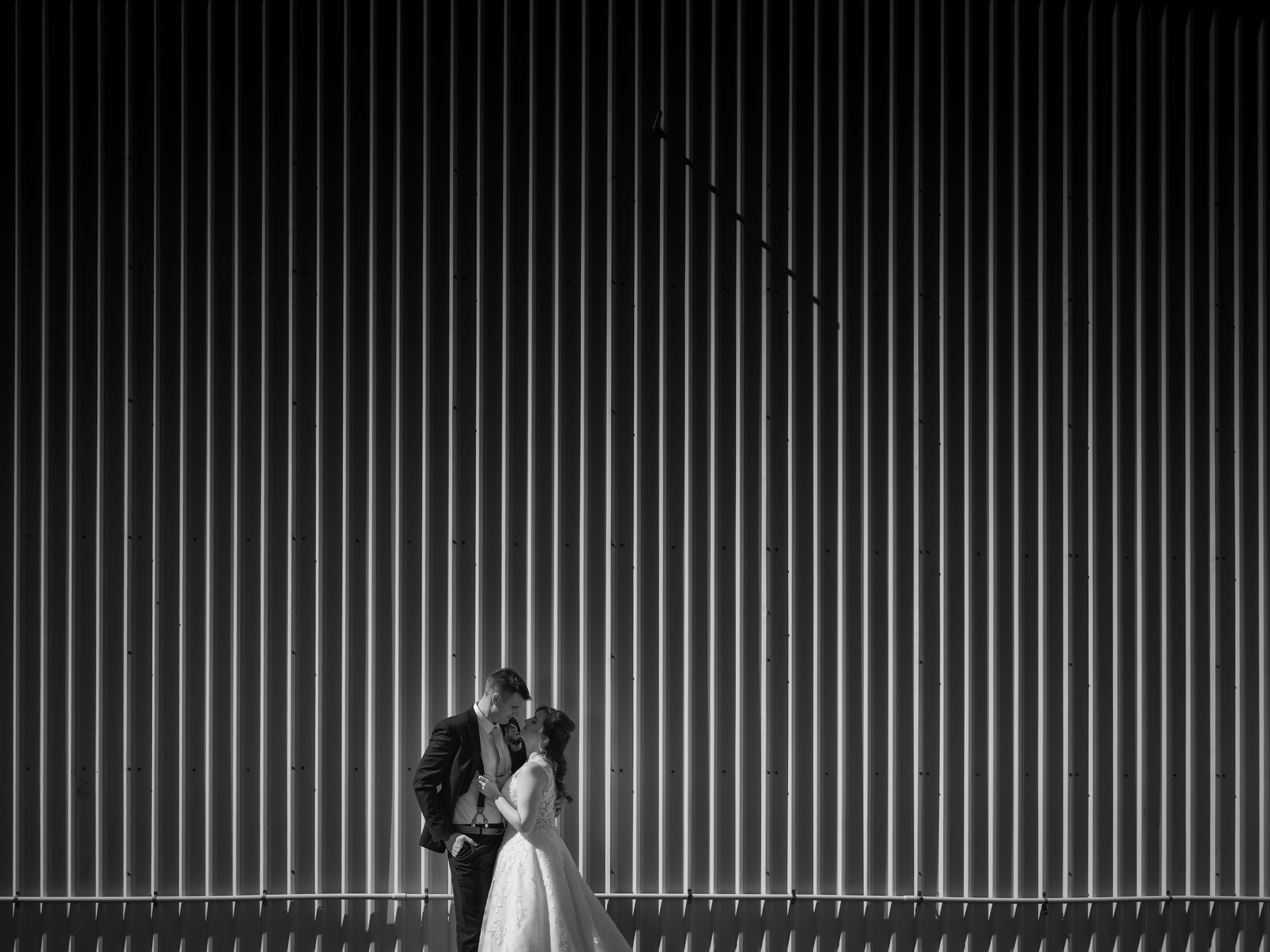 A silhouetted American couple stands in a dramatic black and white corridor with vertical lines creating strong geometric patterns.