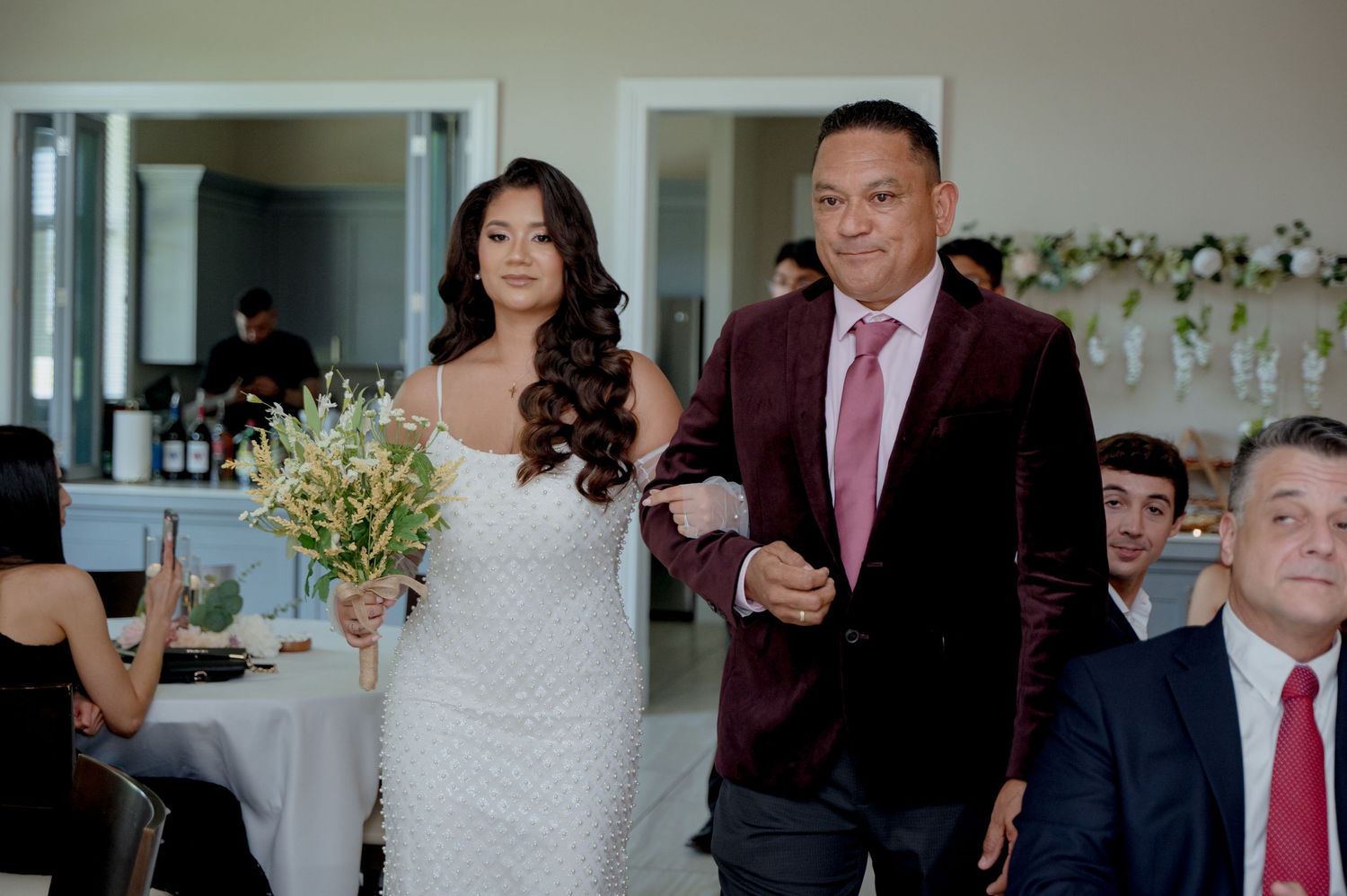 A couple at a wedding reception in formal attire with festive indoor seating and decor.