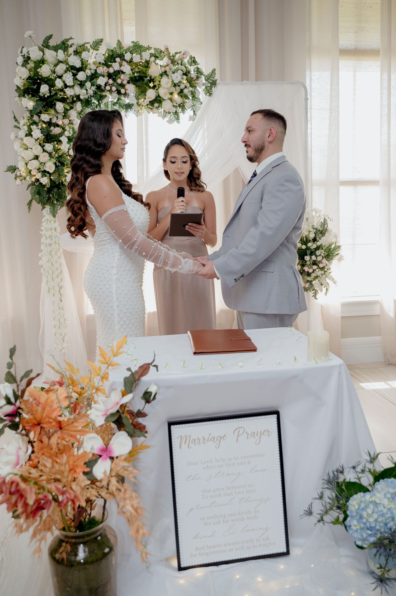 A joyful wedding ceremony moment captured in a bright white room adorned with floral arrangements and decorative elements.