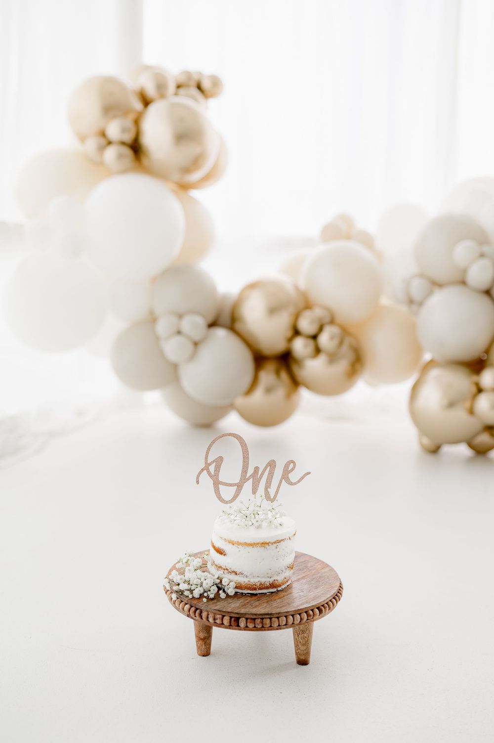 Elegant rose gold wedding rings displayed on white miniature pedestals with ethereal white balloon decor in the background.