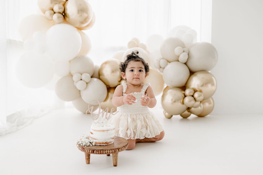 Cream colored balloon garland and decorative setup with wooden furnishings against white backdrop.