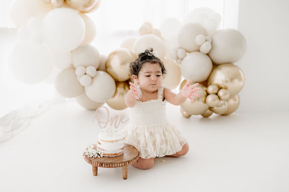 Soft beige and cream balloon arch decorating a dessert table with neutral cake stands and white tableware.