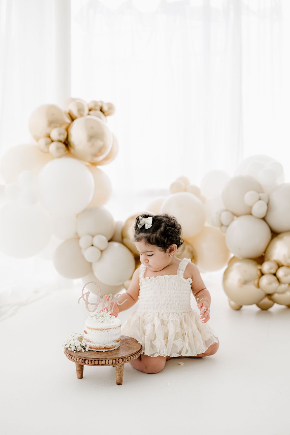 White balloon arch backdrop creates dreamy atmosphere for baby cake smash photography session.