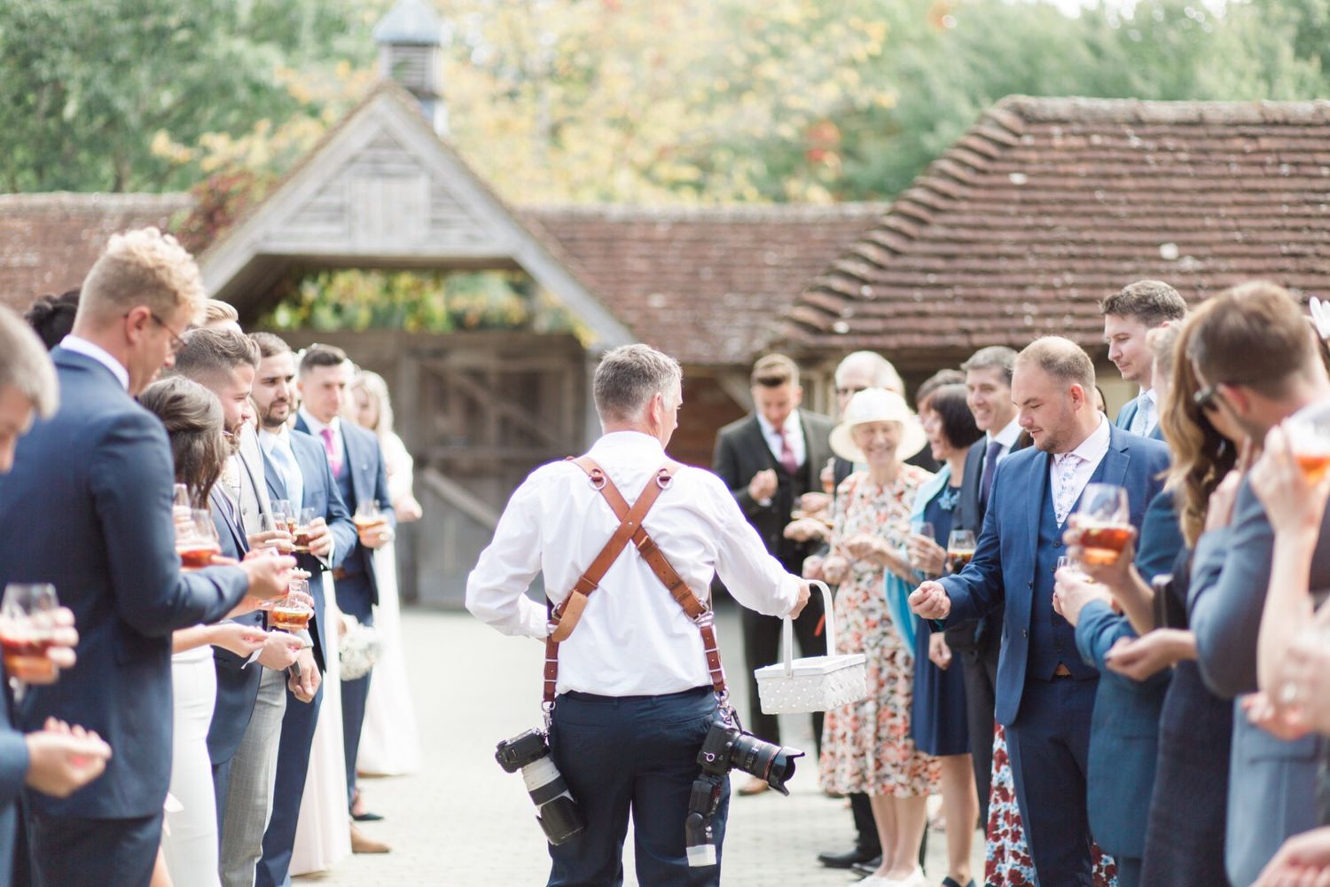 Wedding photographer with dual cameras working among guests at outdoor venue.