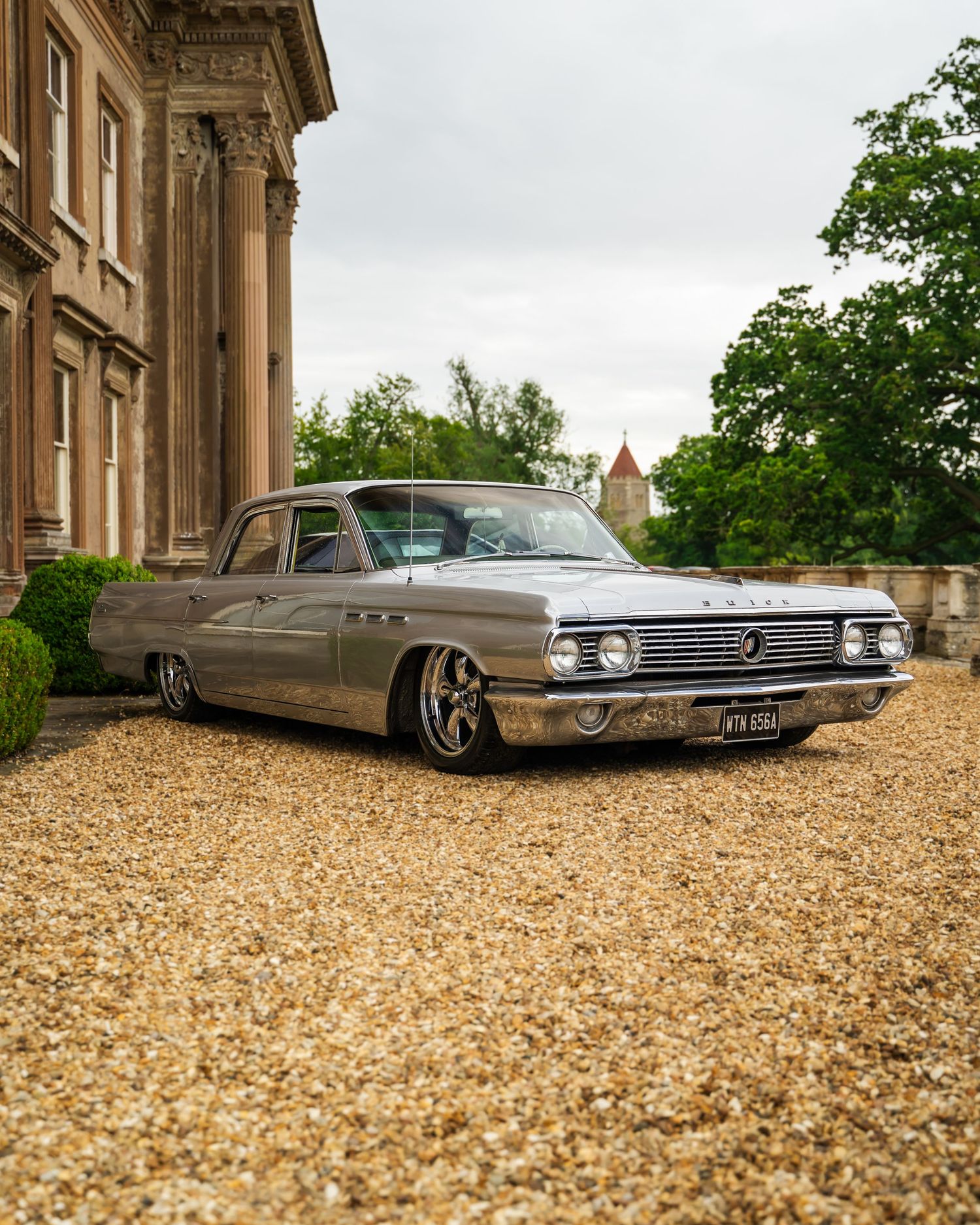 Classic vintage cars parked on gravel in front of a historic stone building.