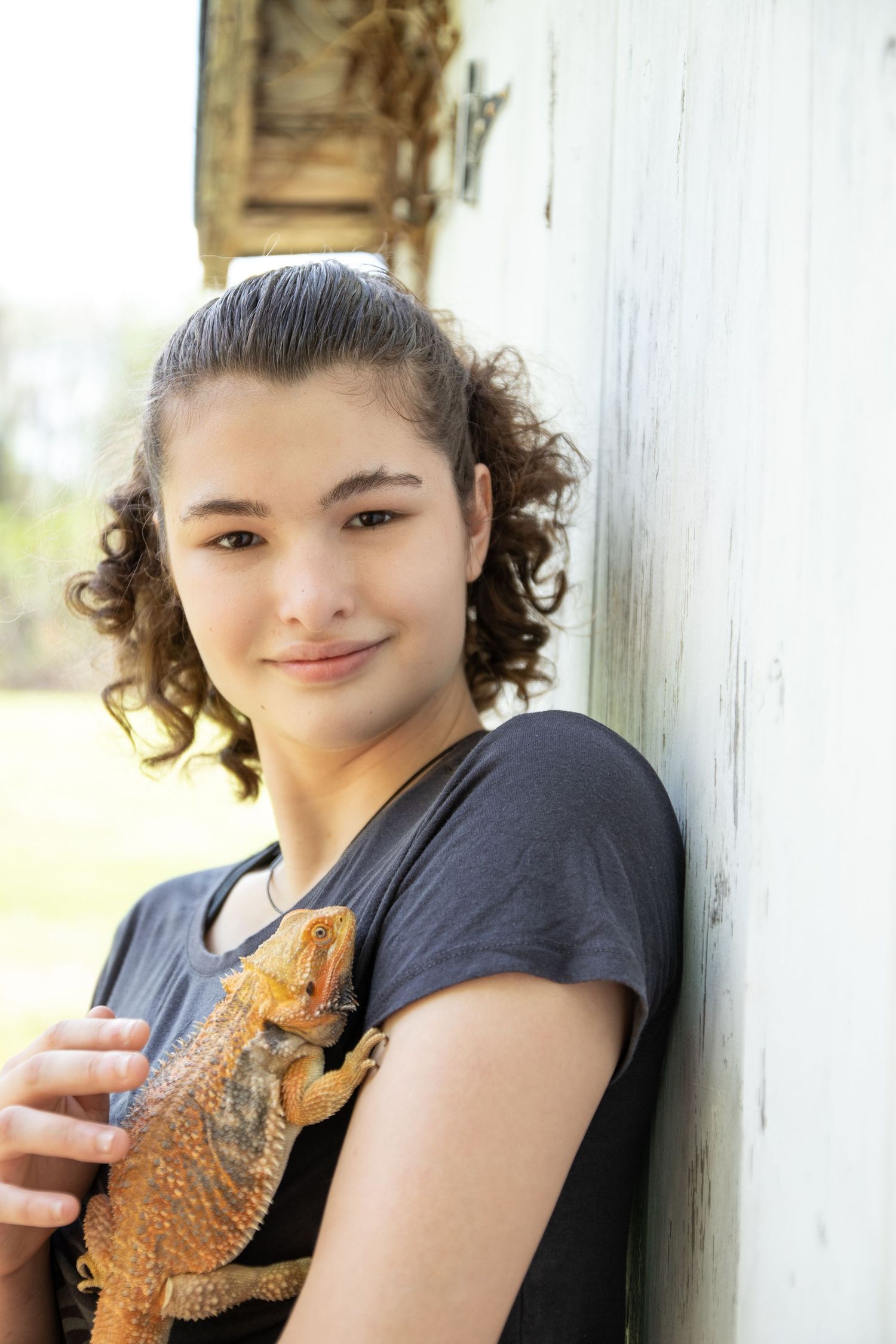 Senior portrait of a girl with autism as she holds a bearded dragon lizard while posing against a white wall outdoors in natural light in CT