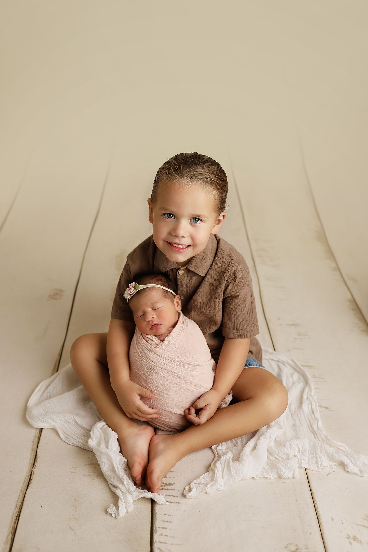 A series of four soft, minimalist newborn photos shows tender sibling interactions on a white backdrop.